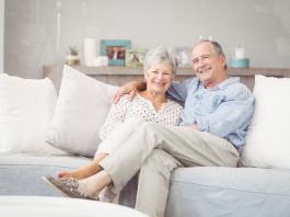 Casal de idosos que trabalham com marketing de rede estão sentados confortavelmente no sofá de uma casa elegante.