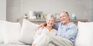 Casal de idosos que trabalham com marketing de rede estão sentados confortavelmente no sofá de uma casa elegante.