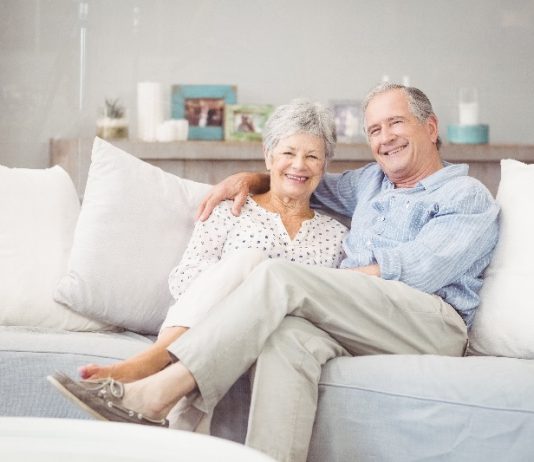 Casal de idosos que trabalham com marketing de rede estão sentados confortavelmente no sofá de uma casa elegante.