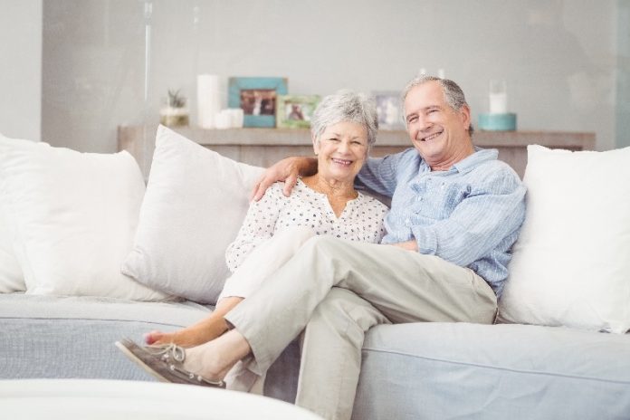 Casal de idosos que trabalham com marketing de rede estão sentados confortavelmente no sofá de uma casa elegante.