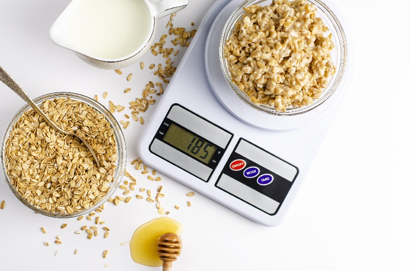 Balança digital de cozinha está pesando uma tigela cheia de cereais.