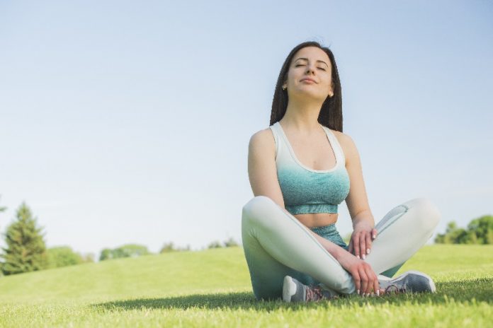 Mulher sentada de pernas cruzadas num parque, reflete após fazer exercícios e isso é bom para a saúde.