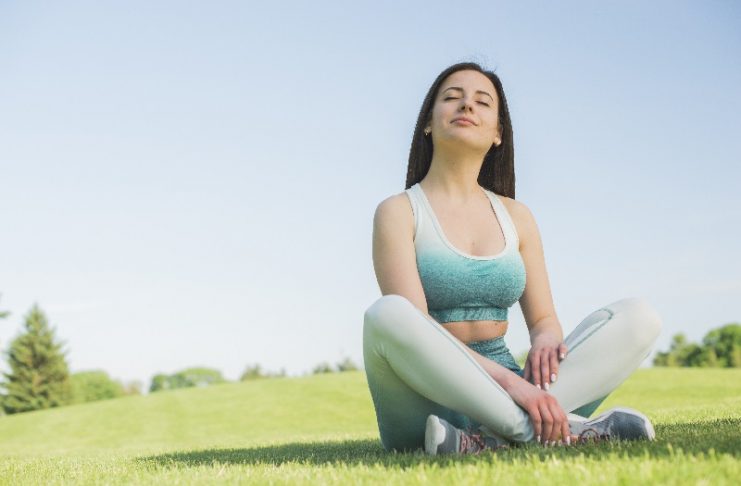 Mulher sentada de pernas cruzadas num parque, reflete após fazer exercícios e isso é bom para a saúde.