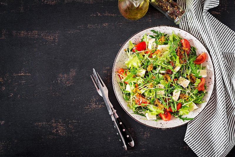 Um prato de salada de legumes e verduras bem colorido aparece ao lado dos talheres.