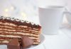 Uma deliciosa fatia de bolo é servida acompanhada de dois corações de chocolate. Uma xícara branca aparece ao fundo.