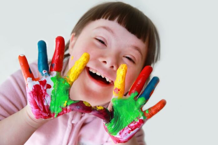 Menina com Síndrome de Down mostrando a palma das mãos, quem estão pintadas com tintas após uma atividade lúdica.