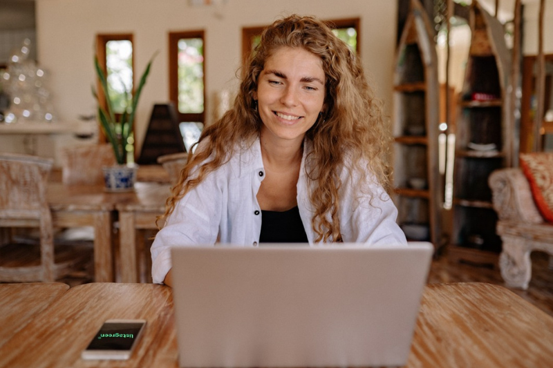 Mulher está na sua mepresa, trabalhando no laptop e sorrindo por participar da Lista Green